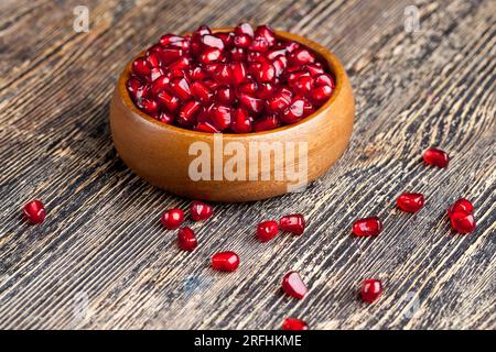 Roter reifer Granatapfelsamen auf einem Teller, geschälter roter Granatapfel auf einer Holzplatte auf dem Tisch Stockfoto