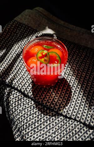 Blick aus einem hohen Winkel auf die erfrischende Wassermelone agua Fresca Getränk mit jalapeño und Wassermelonenkugeln auf schwarzem und weißem Tuch in der Sonne Stockfoto