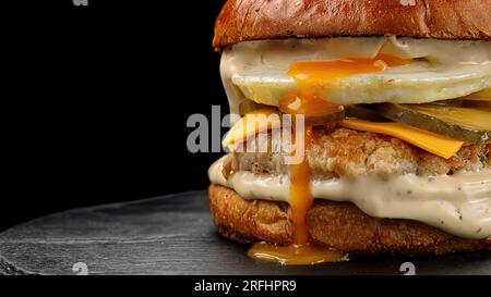 Burger mit Hühnerpatty, Ei und Käse, auf schwarzem Hintergrund Stockfoto