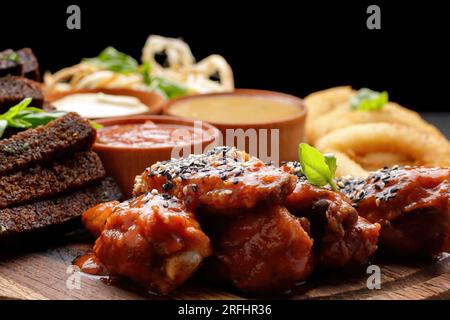 Eine Auswahl an Biervorspeisen mit verschiedenen Saucen auf einem Holzbrett. Calamari, Grillflügel, Knoblauch-Croutons Stockfoto