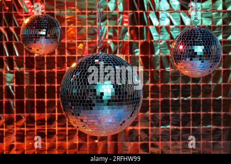Glänzende Disco-Bälle gegen einen Partyvorhang unter farbigen Lichtern Stockfoto