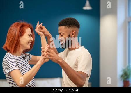 Liebevolles junges, vielfältiges Paar, das romantischen Tanz im modernen Schlafzimmer mit Panoramafenstern tanzt. Stockfoto