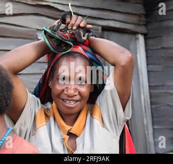 Eine Nahaufnahme einer jungen Frau mit Händen auf dem Kopf vor einem Holzhaus, das bereit ist, auf den Markt in den Hochländern von Papua, Indonesien, zu gehen. Stockfoto