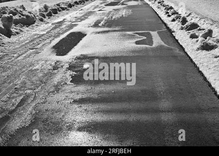 Schmelzen von Schnee und Eis auf asphaltierter, leerer Straße, sonniger Tag Gegenlicht, in Schwarz und Weiß Stockfoto