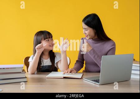 Eine schöne und nette asiatische Lehrerin unterrichtet Mathematik an einem niedlichen kleinen Mädchen am Lerntisch und zählt die Zahlen zusammen. Isolierter gelber Rücken Stockfoto
