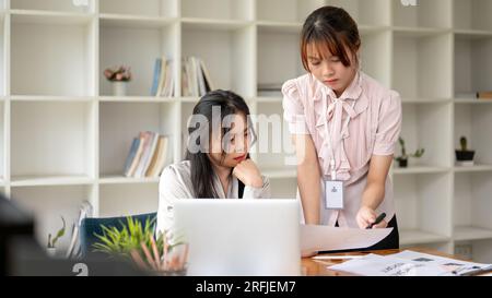 Zwei konzentrierte und professionelle asiatische Geschäftsfrauen oder Buchhalterinnen diskutieren über die Arbeit, analysieren Vertriebsdaten und arbeiten im Büro, um zu arbeiten Stockfoto