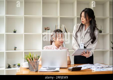 Zwei konzentrierte asiatische Geschäftsfrauen oder Buchhalterinnen diskutieren über die Arbeit, analysieren Vertriebsdaten und arbeiten gemeinsam im Büro. Stockfoto