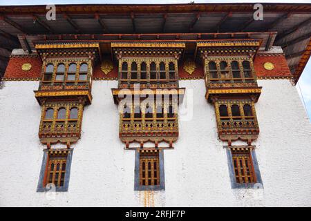 Drei Blöcke dekorativer, traditionell bemalter Holzfenster reichen von der weiß getünchten Steinwand von Punakha Dzong im Königreich Bhutan Stockfoto