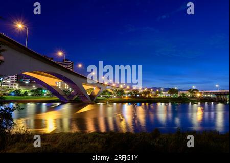 Straßenlichter und Autolichter fließen und reflektieren auf dem See. Romantische Nachtszene. Genießen Sie den sommerlichen Sternenhimmel auf der Milchstraße in Bitan, New Taipei City. Stockfoto