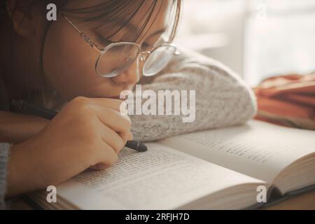 Langweiliges Mädchen, das auf einem Buch liegt und ein Buch liest, Studentenmädchen, das sich müde oder deprimiert fühlt. Stockfoto