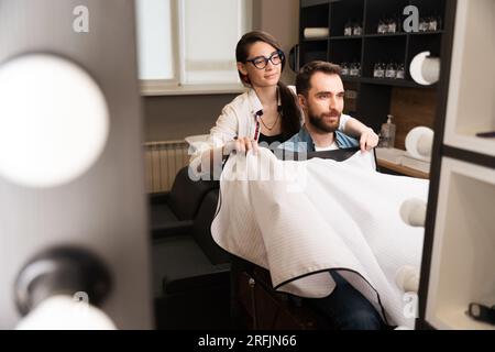 Die Barbierin entfernt den schutzumhang vom Kunden Stockfoto