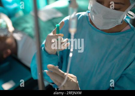 Birassische Chirurg in Operationskittel mit Tropfinfusion im Operationssaal des Krankenhauses Stockfoto