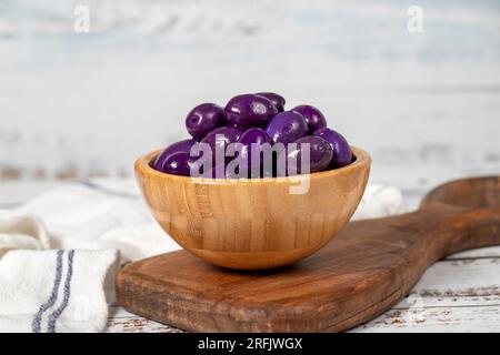 Fermentierte Oliven mit Heidelbeeren in einer Holzschüssel. Lila Oliven auf weißem Holzhintergrund. Mediterrane Küche. Veganes Essen Stockfoto