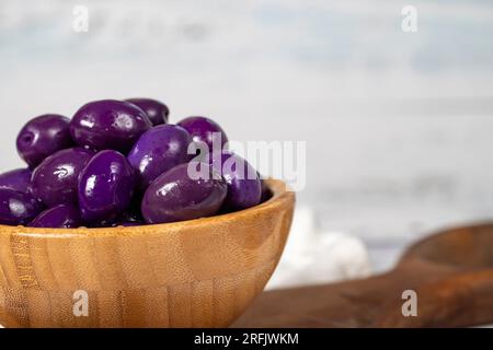 Fermentierte Oliven mit Heidelbeeren in einer Holzschüssel. Lila Oliven auf weißem Holzhintergrund. Mediterrane Küche. Veganes Essen. Speicherplatz kopieren. Leerer Bereich für Text Stockfoto