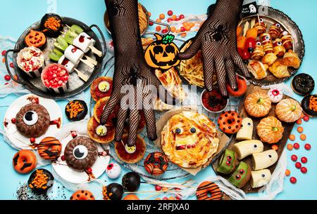 Lustige Halloween-Dinner-Party-Tischszene auf blauem Hintergrund. Draufsicht. Pizza, Kuchen, Spaghetti und Snacks. Stockfoto