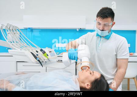 Der Arzt in der Zahnarztpraxis stellt Photopolymerfüllung auf Brünette Stockfoto