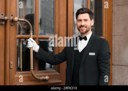 Butler in elegantem Anzug und weiße Handschuhe öffnen die hölzerne Hoteltür Stockfoto