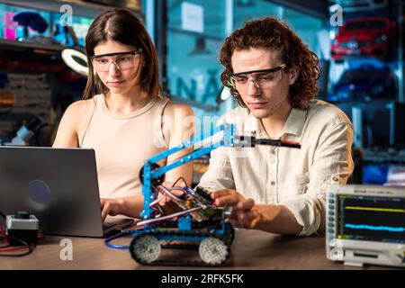 Junger Mann und Frau in Schutzbrille, die Roboterexperimente in einem Labor mit einem Computer durchführen. Roboter und Werkzeuge auf dem Tisch Stockfoto