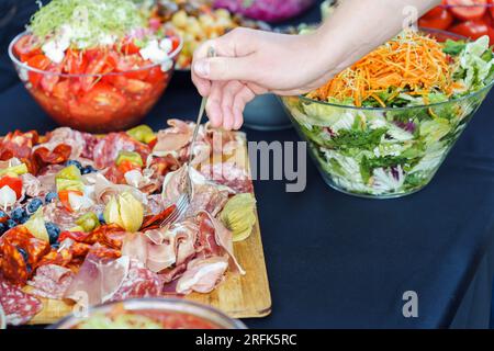 Während einer festlichen Veranstaltung nimmt die Hand Fleischsnacks von der Fleischplatte auf den Büfetttisch Stockfoto