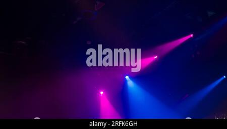 Violette und blaue Lichtstrahlen von Bühnenspots in Rauch auf dunkel verschwommenem Hintergrund, moderne Bühnenbeleuchtungsgeräte Stockfoto