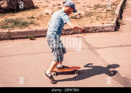 Ein Junge fährt an einem sonnigen Tag auf einer Asphaltstraße Skateboard. Extremsport. Getöntes Foto Stockfoto