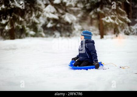 Ein kleiner Junge sitzt auf einer Schneeuntertasse im Winterpark. Bild mit Selektiv. Konzentrier dich Stockfoto