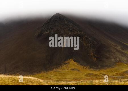 Felsiger schwarzer Vulkanberg mit Gipfel, der nach starkem Regen auf der Halbinsel Snaefellsnes in Snaefellsnes, Island in EA, durch Wolken in niedriger Höhe sichtbar ist Stockfoto