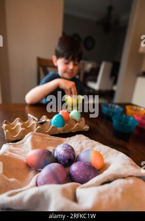 Ein Haufen farbiger ostereier mit einem Jungen, der im Hintergrund ein Ei stirbt. Stockfoto