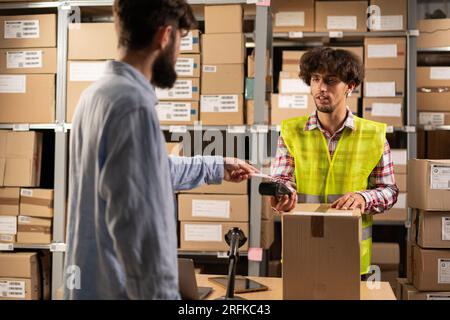 Männliche Kundenzahlung Online-Bestellung am Abholort. Online-Shop-Lager arabischer Mitarbeiter, der dem man-Kunden im Postamt das Paket übergibt Stockfoto