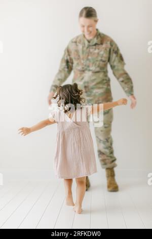 Mädchen in lila Kleid läuft, um militärmutter in Uniform zu umarmen Stockfoto