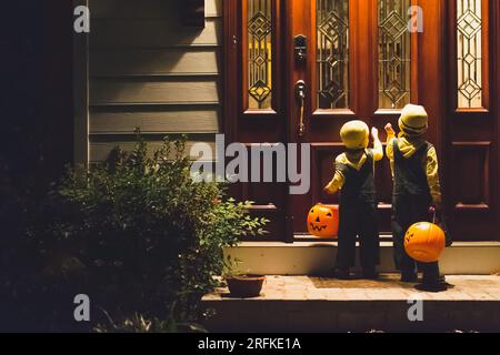 Junge Jungen klopfen an die Haustür, um an Halloween zu tricksen oder zu verwöhnen. Stockfoto