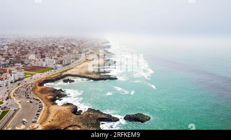 Drohnenansicht von Rabat, Marokko. Felsige Küste des Atlantiks mit Wohngebäuden und Autobahn, Nebel in der Luft Stockfoto