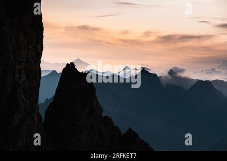 Rötliche Landschaft bei Sonnenuntergang über den Bergen des Ecrins-Massivs in den französischen Alpen mit mehreren Gipfeln zwischen den Wolken Stockfoto