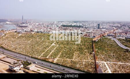 Drohnenansicht von Rabat, Marokko. Märtyrerfriedhof an der felsigen Atlantikküste mit Wohngebäuden in der Ferne Stockfoto