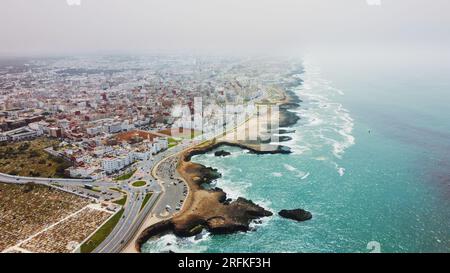 Drohnenansicht von Rabat, Marokko. Felsige Küste des Atlantiks mit Wohngebäuden und Autobahn, Nebel in der Luft Stockfoto