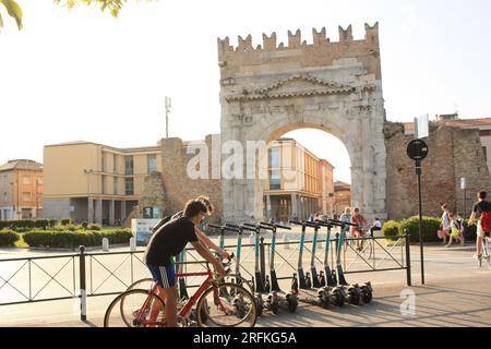 RIMINI, ITALIEN - 15. MAI 2022: Fahrradtour und geparkte Motorroller mit Blick auf den Bogen in Rimini Stockfoto