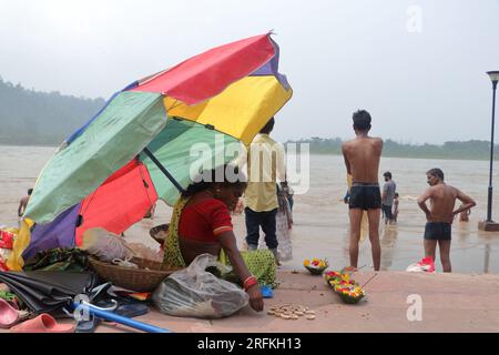 Eine arme Frau, die Puja-Artikel in Triveni Ghat, Rishikesh, verkauft und einen Schirm hält, um sich vor der Sonne zu schützen. Rishikesh. Uttarakhand. Indien. Asien. Stockfoto