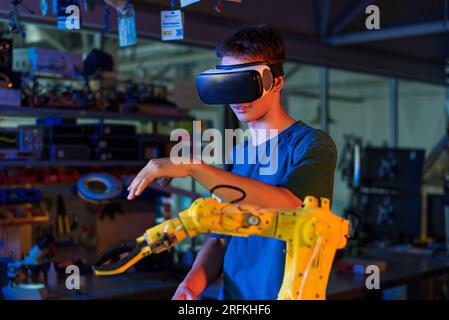 Teenager, die Roboterexperimente in einem Labor machen. Der Junge im VR-Headset steuert den Roboter mit der Hand. Rote und blaue Beleuchtung Stockfoto