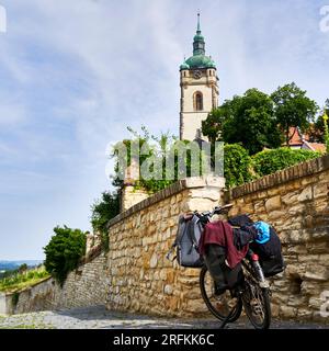 Voll gepacktes Fahrrad auf Kopfsteinpflaster vor einer Steinmauer mit einem Kirchturm im Hintergrund, Tschechische Republik Fahrradtour Stockfoto