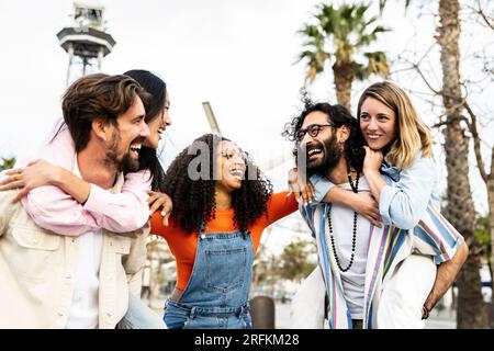 Eine Gruppe multiethnischer Freunde, die Huckepack fahren und sich anschauen. Vielfältige junge Frauen und Männer, die Spaß haben zu lachen und sorglos anstarren Stockfoto