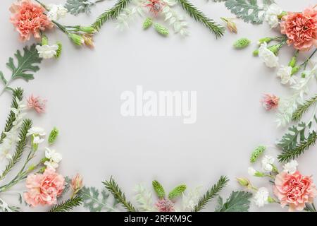 Blütenzusammensetzung aus Korallenkarnation und silbergrünen Blättern von Senecio cineraria auf pastellgrauem Hintergrund. Naturkonzept, Kopierraum, flach l Stockfoto