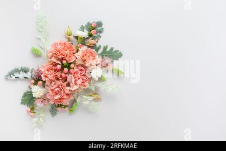 Blütenzusammensetzung aus Korallenkarnation und silbergrünen Blättern von Senecio cineraria auf pastellgrauem Hintergrund. Naturkonzept, Kopierraum, flach l Stockfoto