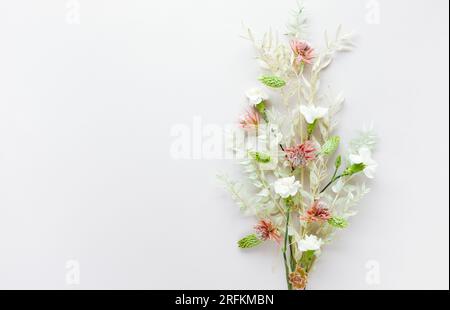 Blütenzusammensetzung aus getrockneten, hellgrünen Blättern von Ruscus und weißen Blüten auf pastellgrauem Hintergrund. Naturkonzept, Kopierraum, flach liegend. Stockfoto