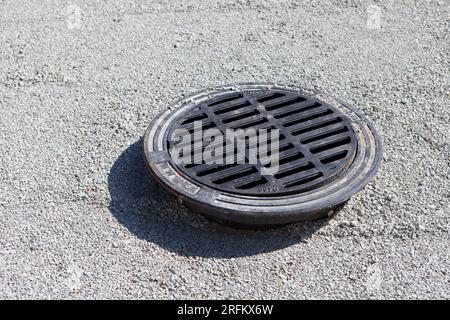 Gusseiserner Schacht auf Kalksteinkieseln, Blick von oben auf die Straße. Straßenbefestigung Am Manhole Stockfoto