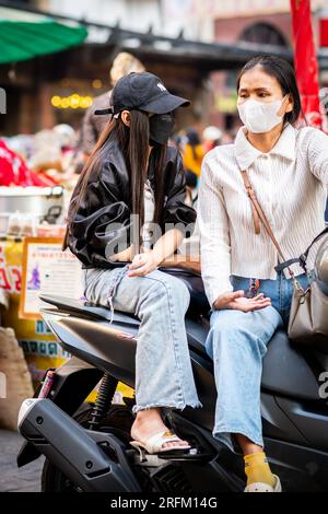 Zwei thailändische Mädchen, die sich tief unterhalten haben, saßen auf ihrem Moped in der Yaowarat Road Markt, China Town, Bangkok Thailand. Stockfoto