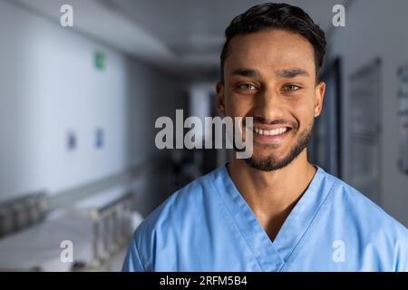 Porträt eines glücklichen, birassischen männlichen Arztes, der im Flur des Krankenhauses Kittel trägt, Kopierraum Stockfoto