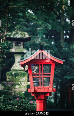 Holzlaterne und Steinlaterne im Wald, Japan. Diese traditionellen Lampen beleuchten häufig Wege zu Shinto-Schreinen oder Tempeln. Stockfoto
