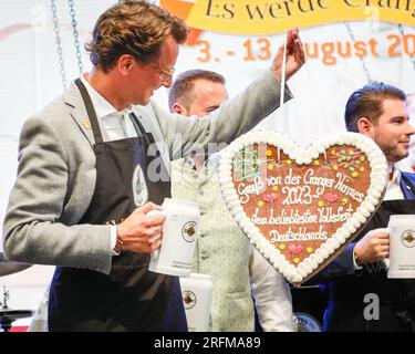 Herne, Deutschland. 04. August 2023. Der Premierminister von Nordrhein-Westfalen, Hendrik Wüst (CDU), erhält ein Lebkuchenherz, während er sich im festlichen Zelt befindet, um das Cranger Kirmes-Messegelände in Herne offiziell zu eröffnen. Die Cranger Kirmes ist eine der größten in Deutschland. Popsängerin Michelle und andere treten auf. Die beliebte Messe zieht während ihres 10-tägigen Laufs regelmäßig mehr als 4m Besucher an. Die Messe stammt aus dem frühen 18. Jahrhundert in Crange. Kredit: Imageplotter/Alamy Live News Stockfoto