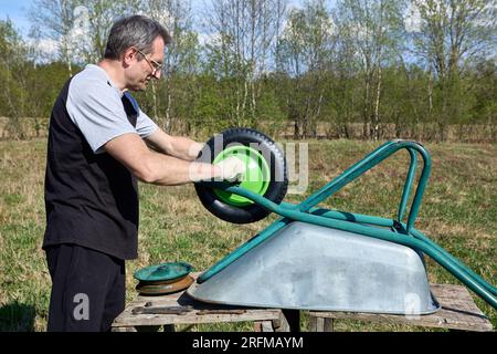 Das pneumatische Rad der Gartenradkarre wurde durch ein neues ersetzt, der Gärtner zieht die Befestigungsmutter fest. Stockfoto