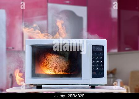 Elektrischer Brand durch defekte Mikrowelle mit Rauch und offenen Flammen in der Küche. Stockfoto